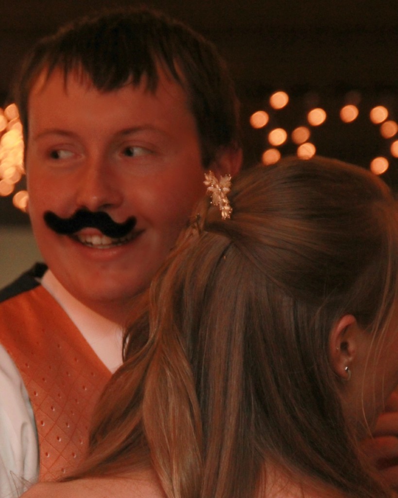 bride and groom dancing while groom wears fake mustache