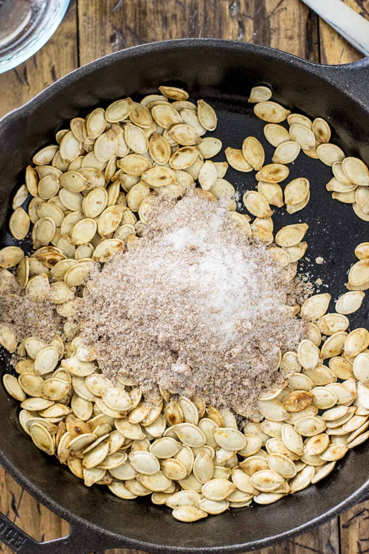 Pumpkin seeds in a skillet, seasoning over top of them