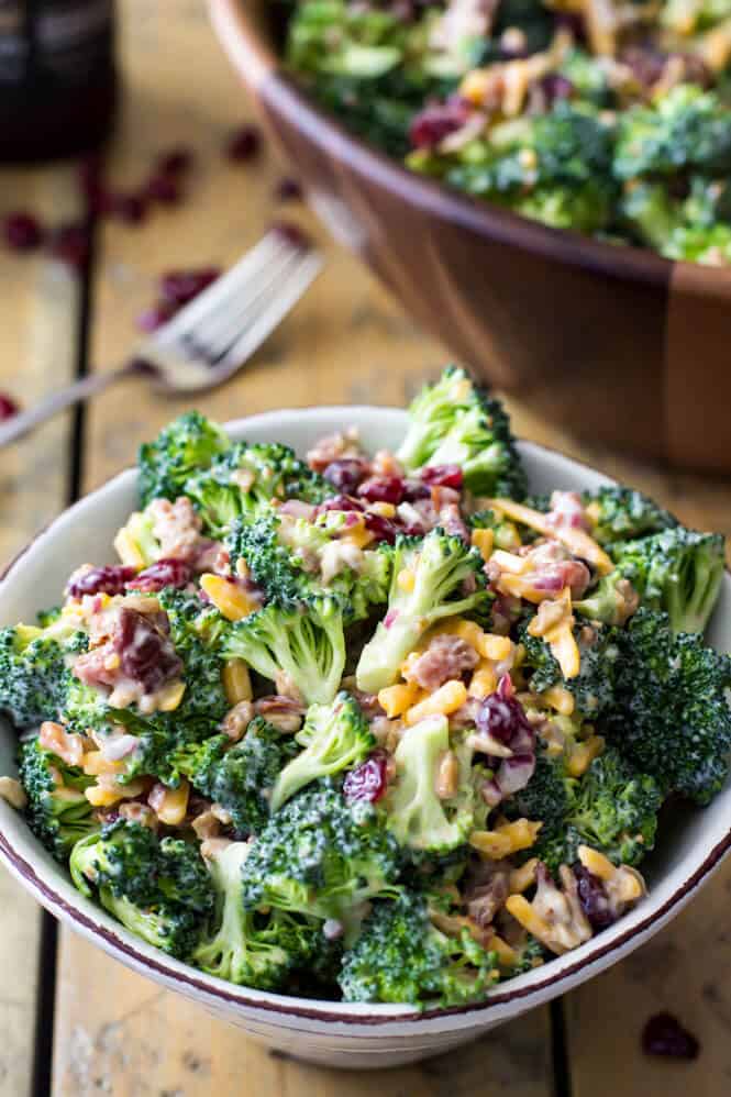 An easy and delicious BROCCOLI SALAD with bacon and cheese! This recipe is always a hit! Easy to make and packed with flavor! #summerfood #potluck White bowl filled with broccoli salad with bacon