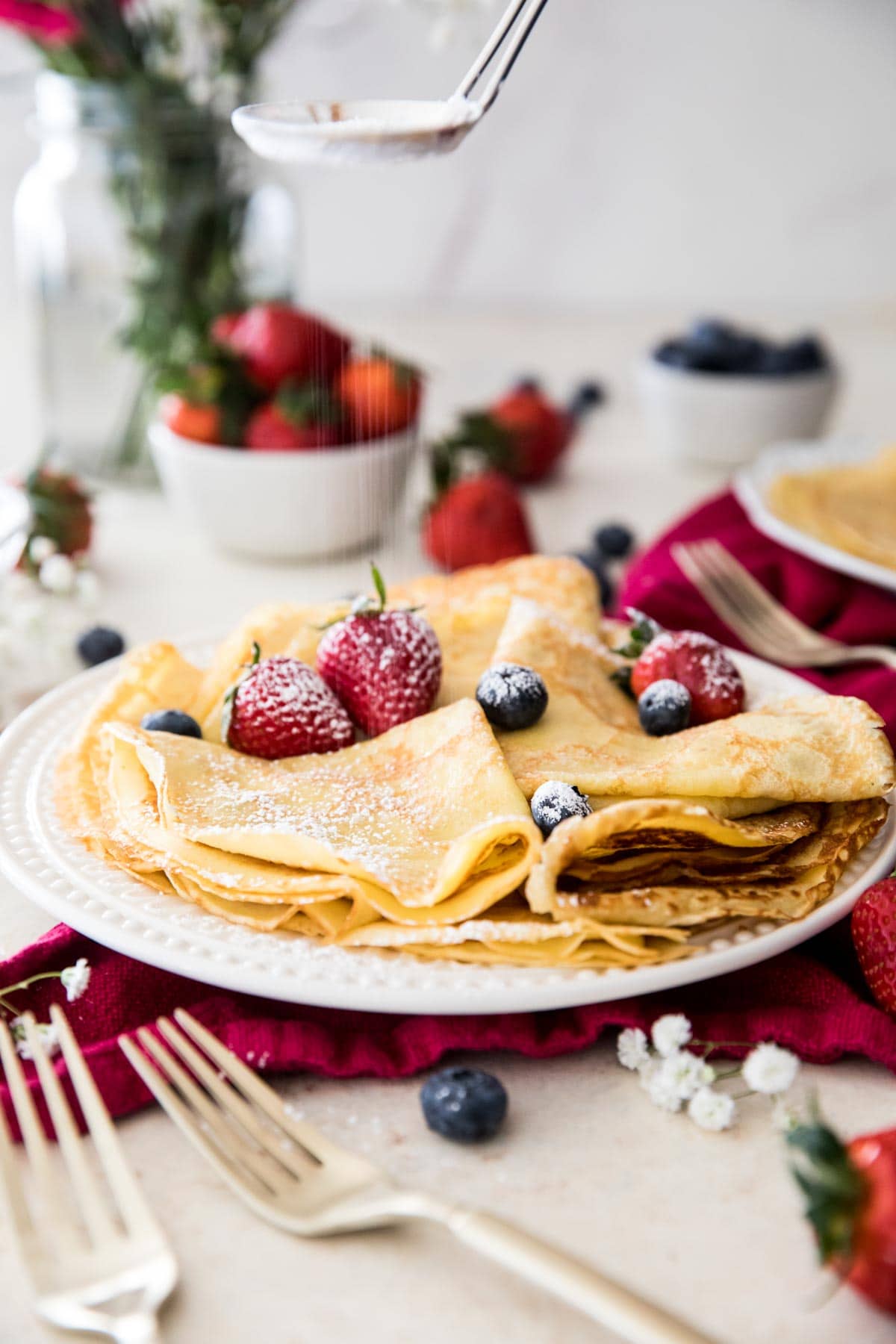 folded up crepes on white plate topped with fruit