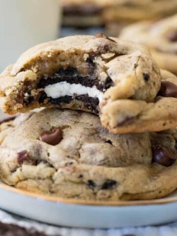 Stack of Oreo stuffed chocolate chip cookie - with bite missing to reveal oreo cookie inside - on plate