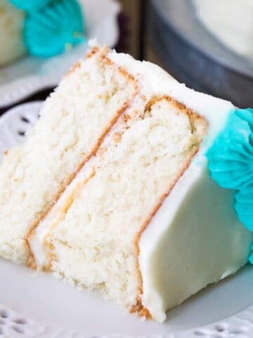 Slice of white cake with white icing and blue icing decorations on plate