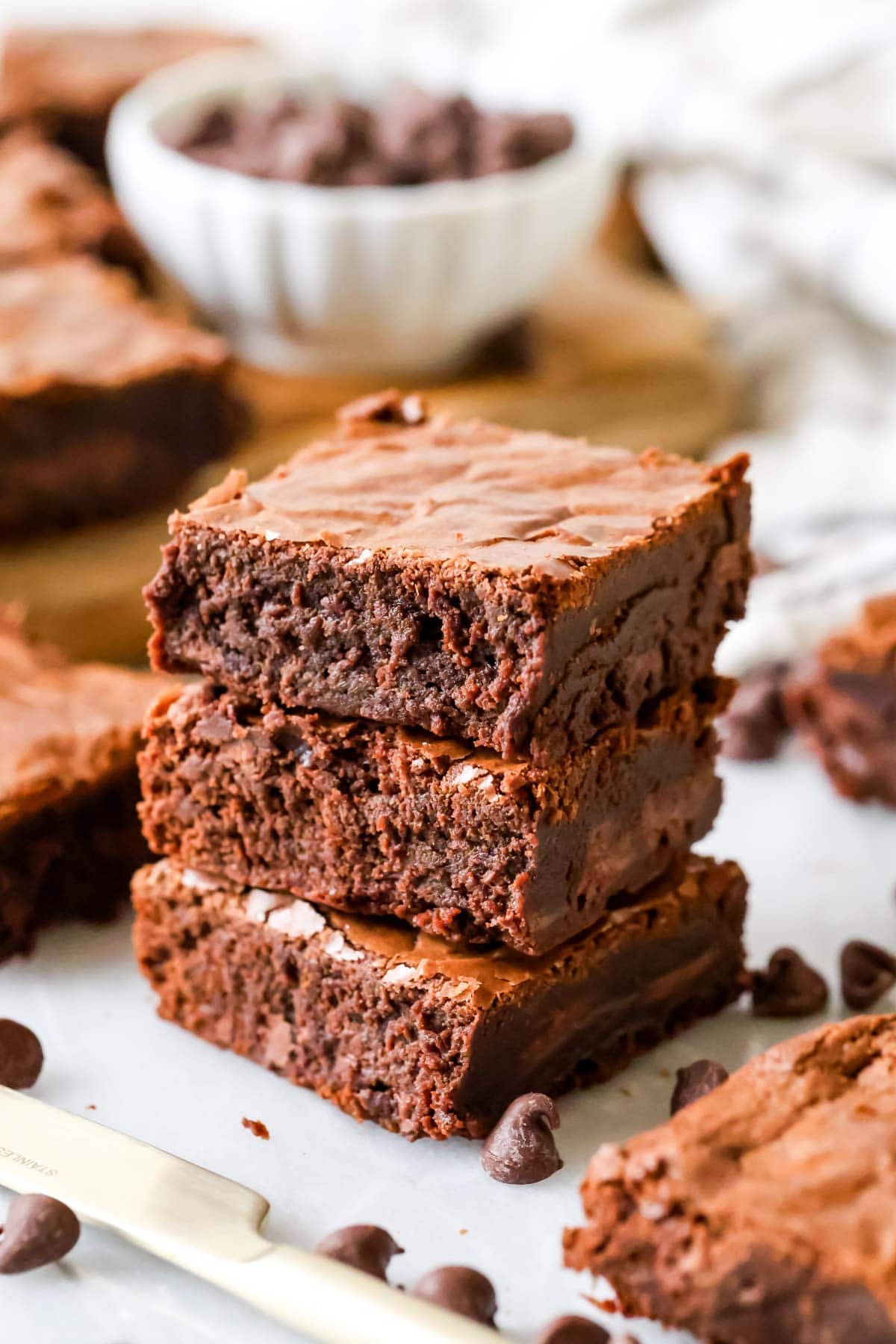 Stack of homemade brownies on marble with white bowl of chocolate chips in background.