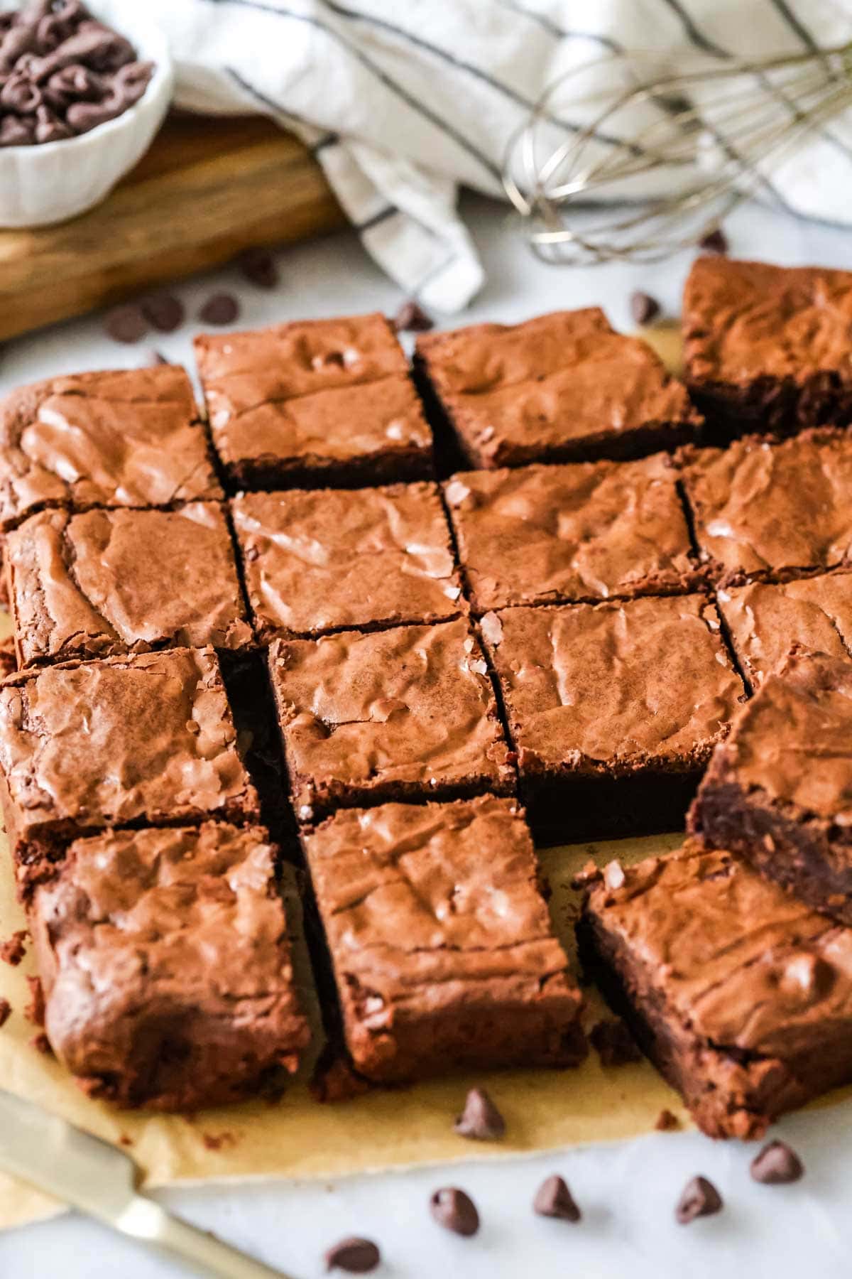 Shiny chocolate brownies cut into squares with chocolate chips and lined towel in background.