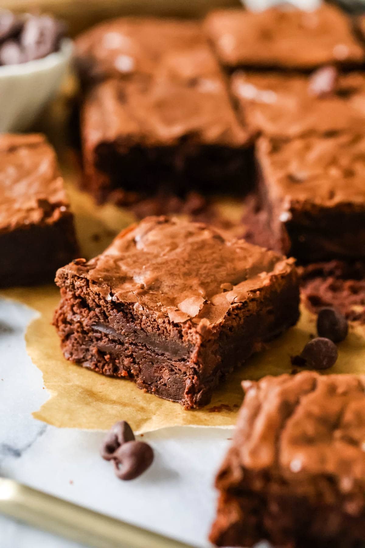 Fudgy homemade brownie square on a piece of parchment, surrounded by more brownie squares.