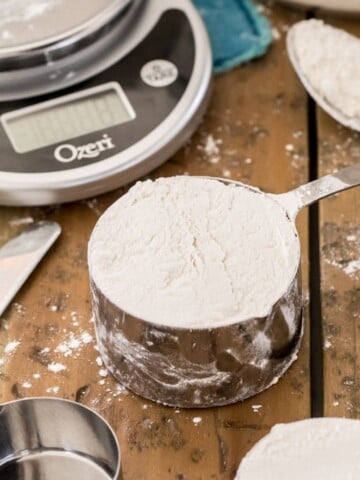 cup of flour on wood surface with scale in background
