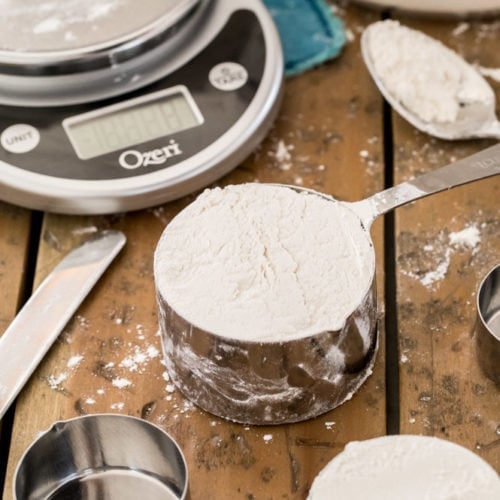 cup of flour on wood surface with scale in background