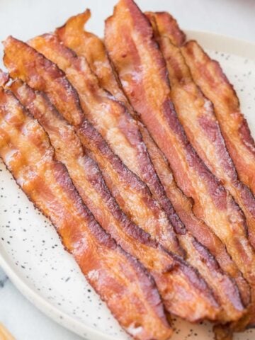 Strips of bacon in the oven on a round speckled white plate