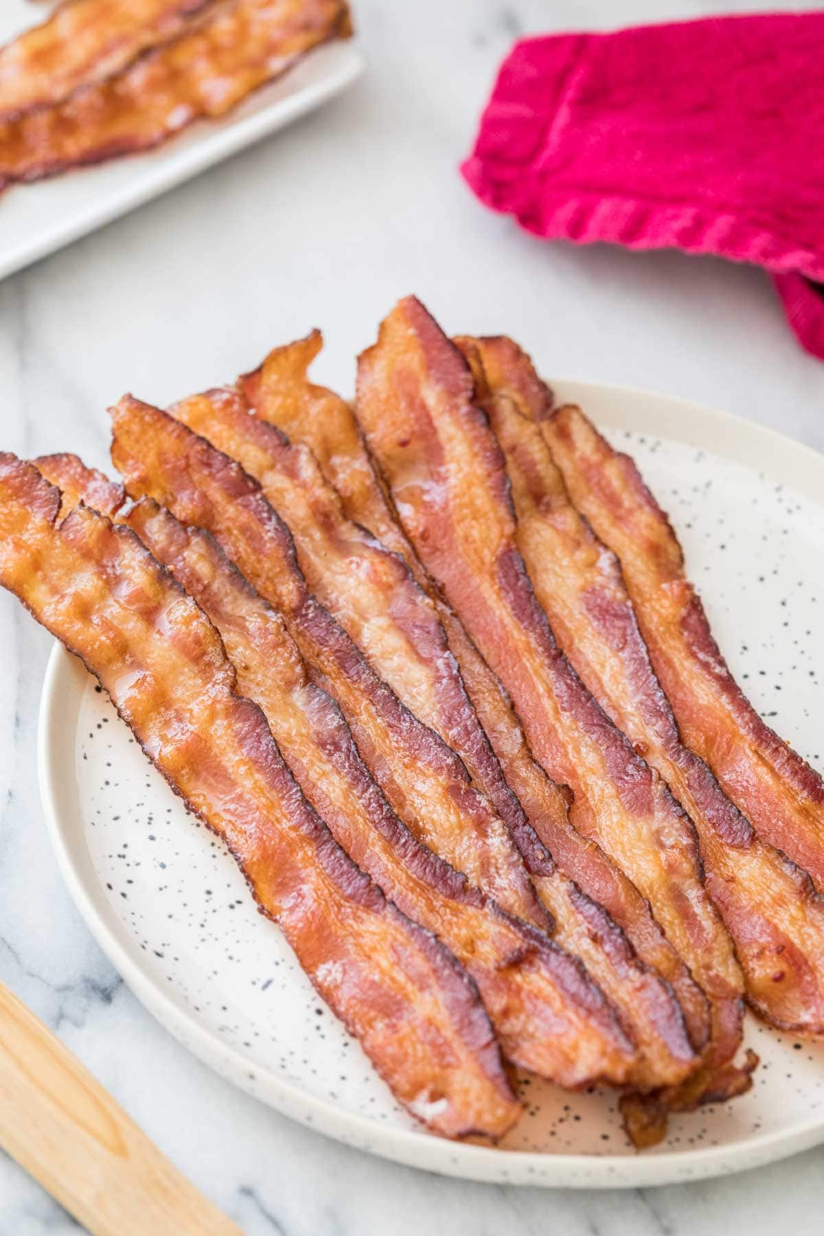 Strips of bacon in the oven on a round speckled white plate