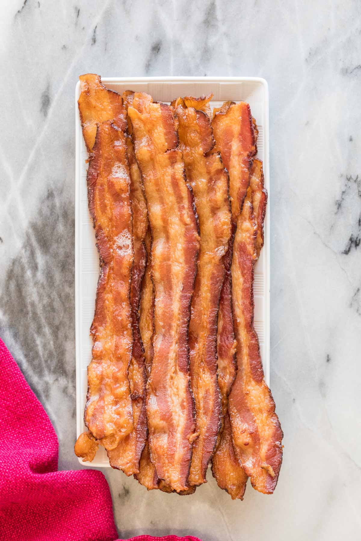Overhead view of strips of crisp bacon arranged on a rectangular white platter