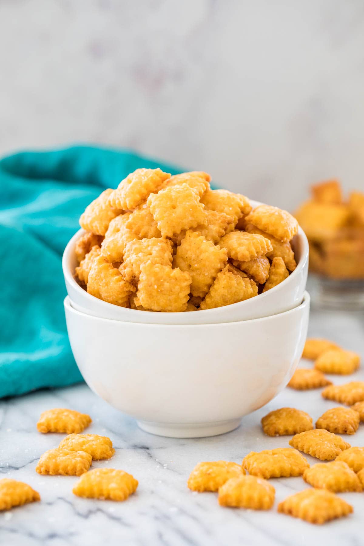 Homemade cheese crackers in stacked white bowls with more crackers scattered underneath