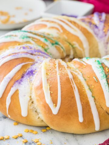 golden brown king cake frosted with white icing and sprinkled with colorful sanding sugars