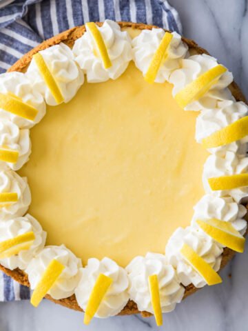 overhead view of a whole lemon cheesecake decorated with whipped cream and lemon slices