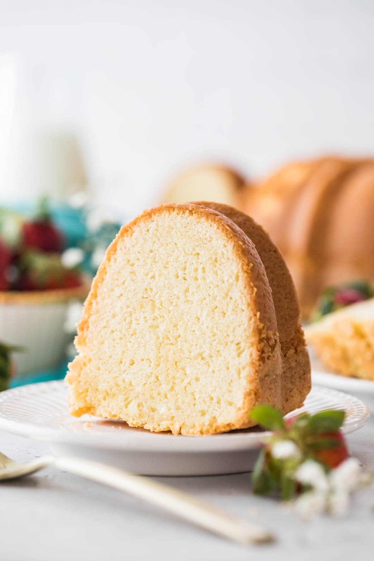 slice of pound cake on a white plate with the remaining cake in the background