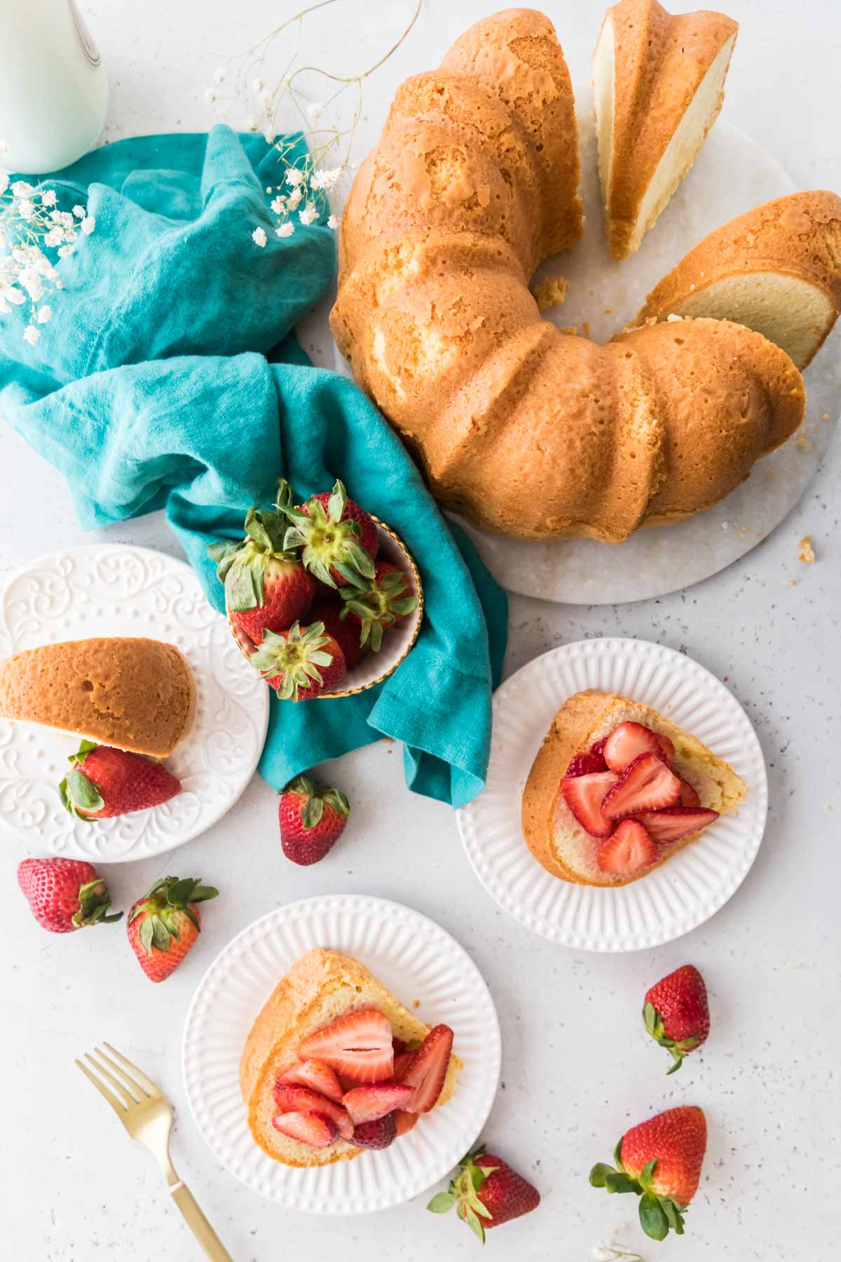 overhead view of a pound cake that's been sliced and served on white plates with a macerated strawberry topping
