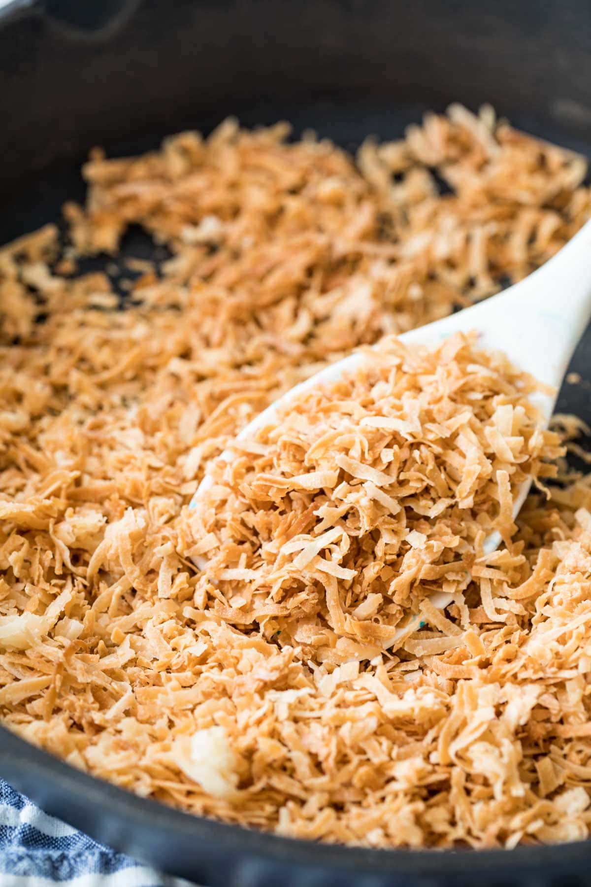 spoon scooping golden brown coconut flakes that have been toasted in a cast iron skillet on the stove