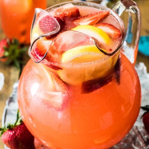 large glass pitcher of homemade strawberry lemonade with sliced strawberries and lemons as a garnish