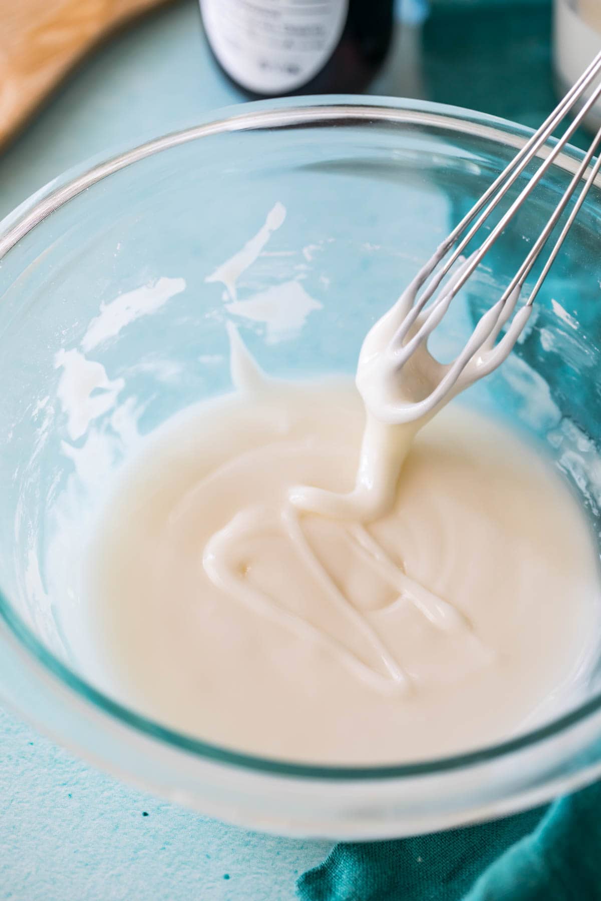 whisk lifting out of a thin glaze in a glass bowl