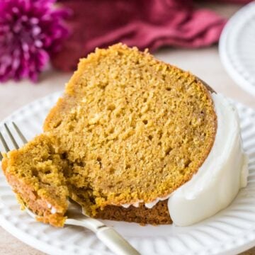 Slice of pumpkin bundt cake topped with cream cheese glaze on a plate with a fork taking one bite.