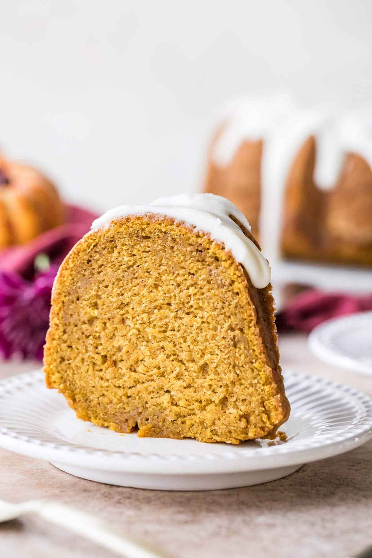 Slice of bundt cake topped with a thick white glaze standing up on a white plate.