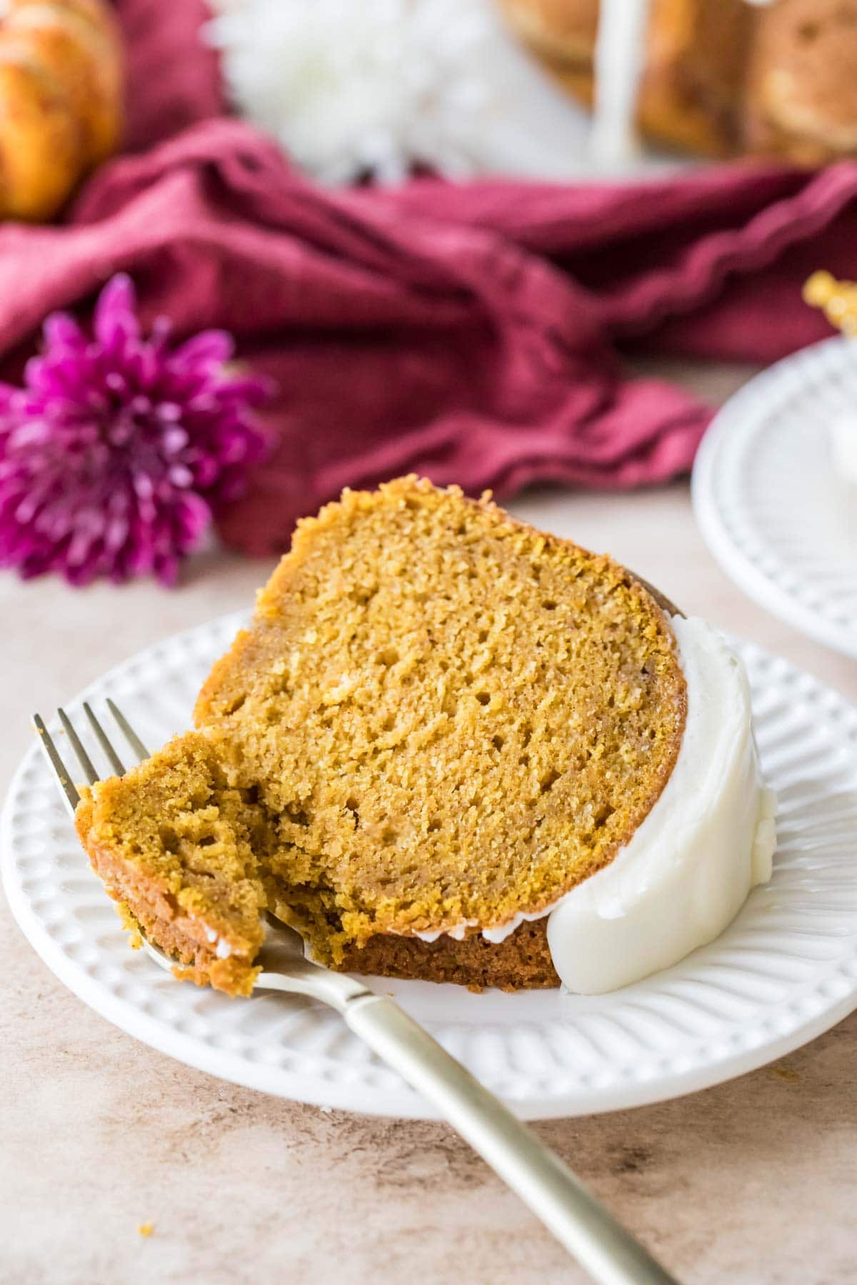 Slice of pumpkin bundt cake topped with cream cheese glaze on a plate with a fork taking one bite.