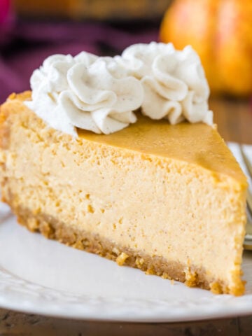 Slice of pumpkin cheesecake topped with cinnamon whipped cream on a white plate.
