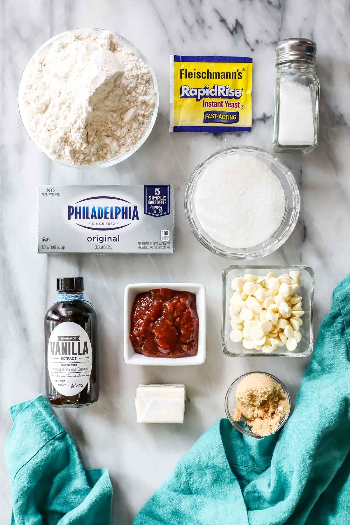 Overhead view of ingredients including yeast, cream cheese, white chocolate chips, raspberry jam, and more.