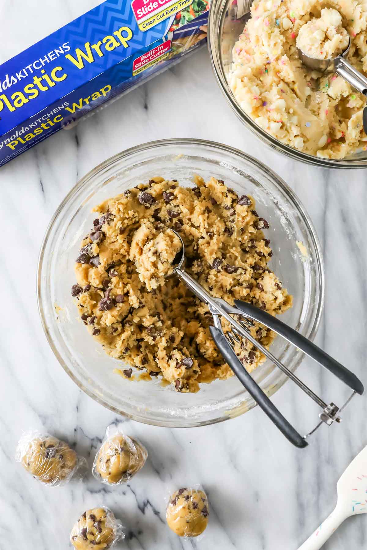 Overhead view of a bowl of chocolate chip cookie dough with a cookie scoop in it.