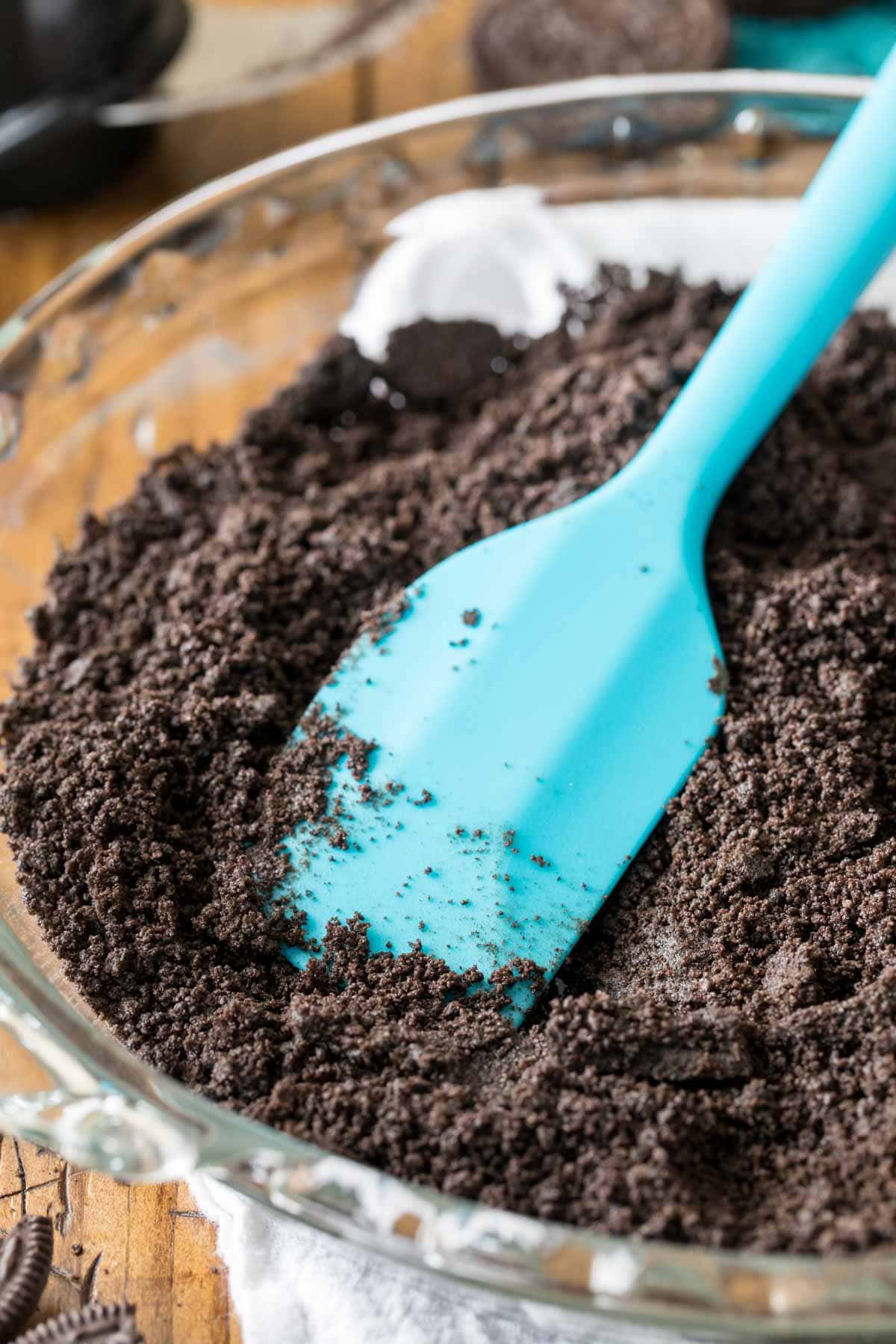 Spatula smoothing Oreo crumbs into a glass pie plate.