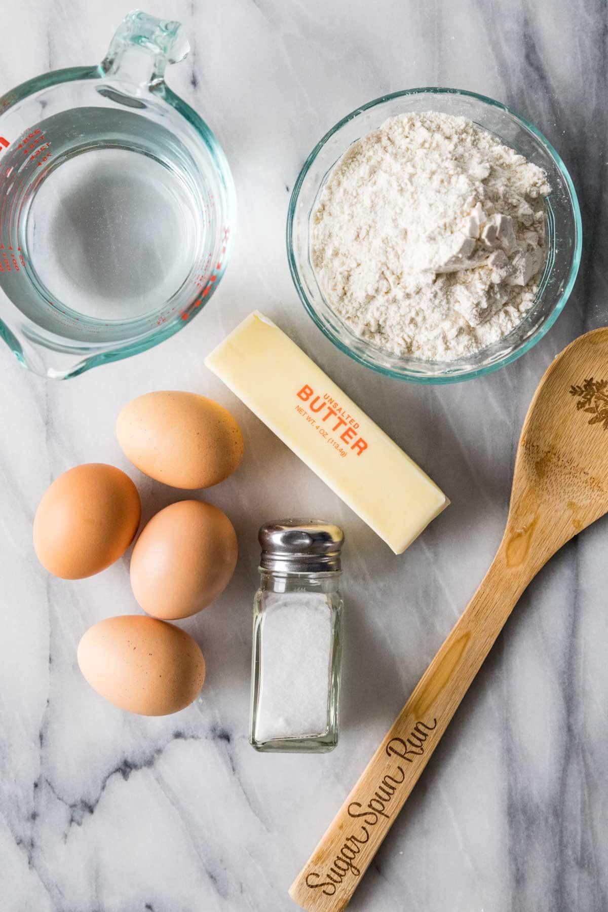 Overhead view of ingredients including water, flour, eggs, butter, and salt.