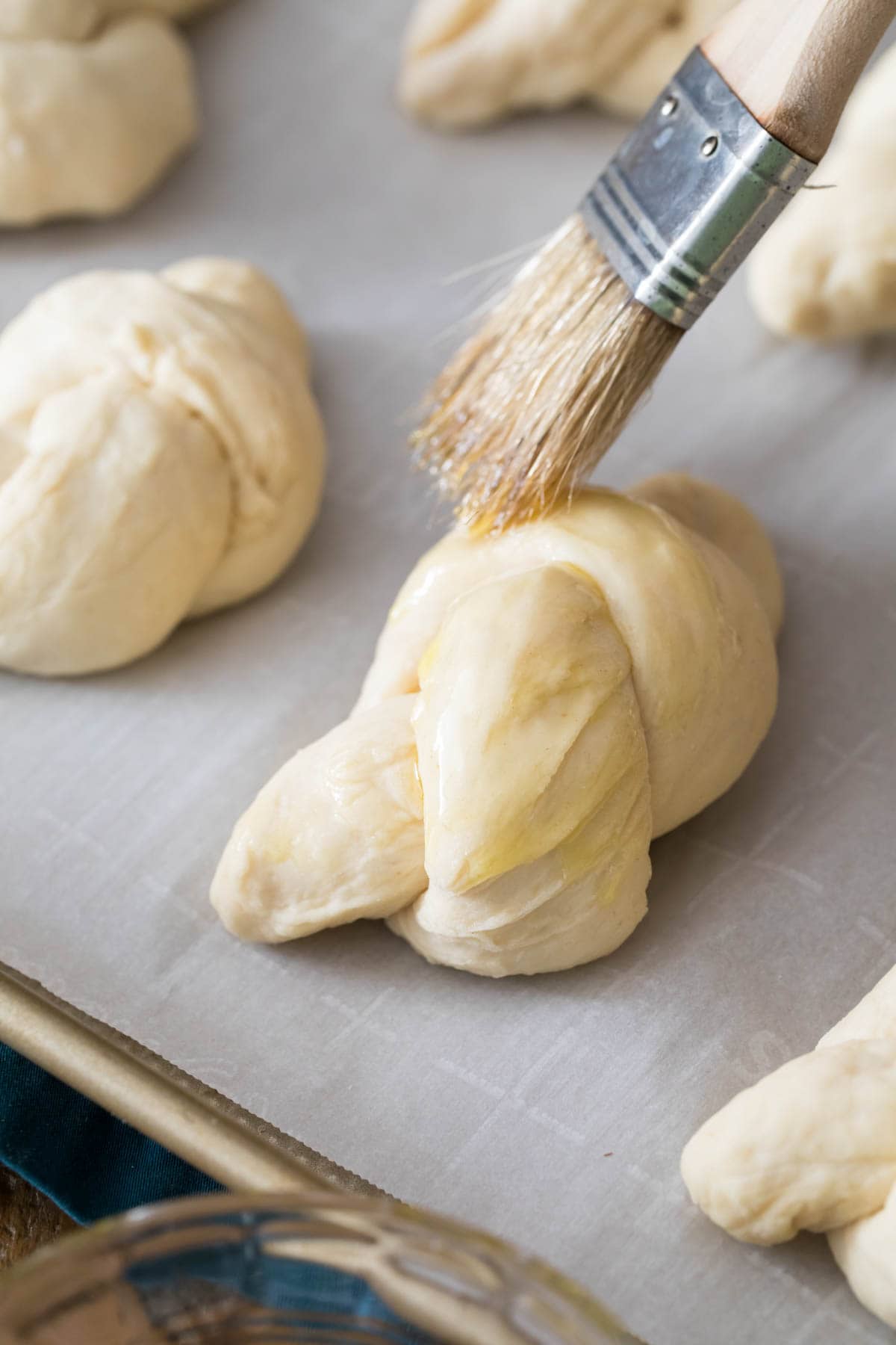 Olive oil being brushed onto bread knots before baking.