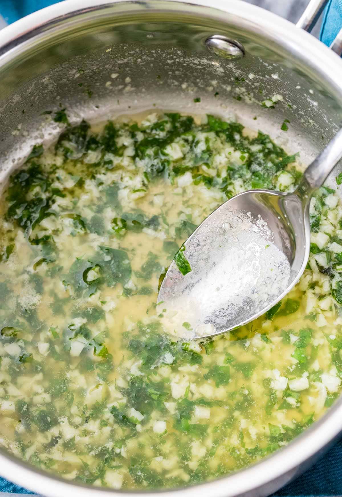 Overhead view of a garlic butter sauce in a metal saucepan.