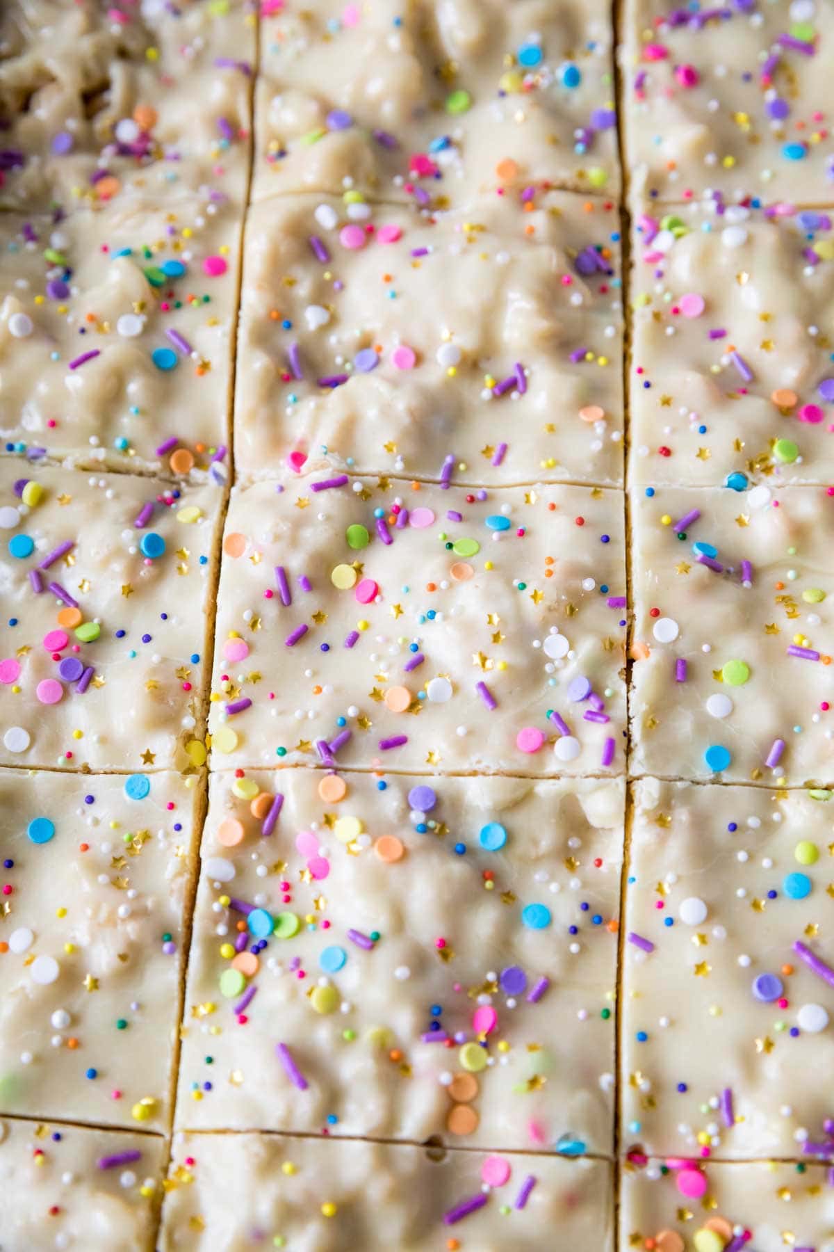 Close-up view of rice krispie treats topped with a fudgy cake batter frosting and rainbow sprinkles.