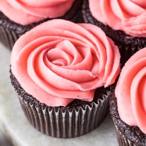 Piped rosettes of raspberry buttercream frosting on top of chocolate cupcakes.