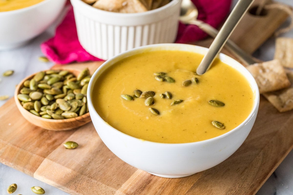 Bowl of soup made from butternut squash with pepitas on top and in a dish to the side.