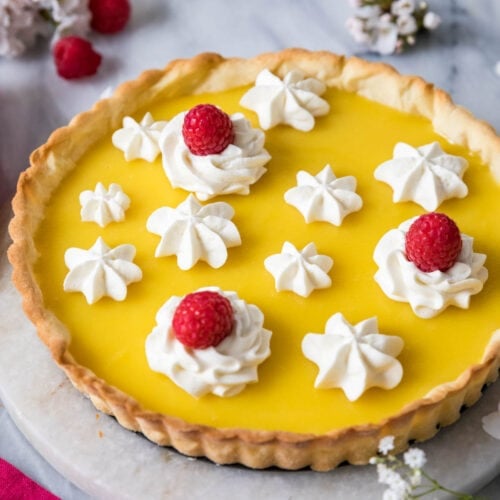 Lemon tart decorated with piped whipped cream and raspberries.