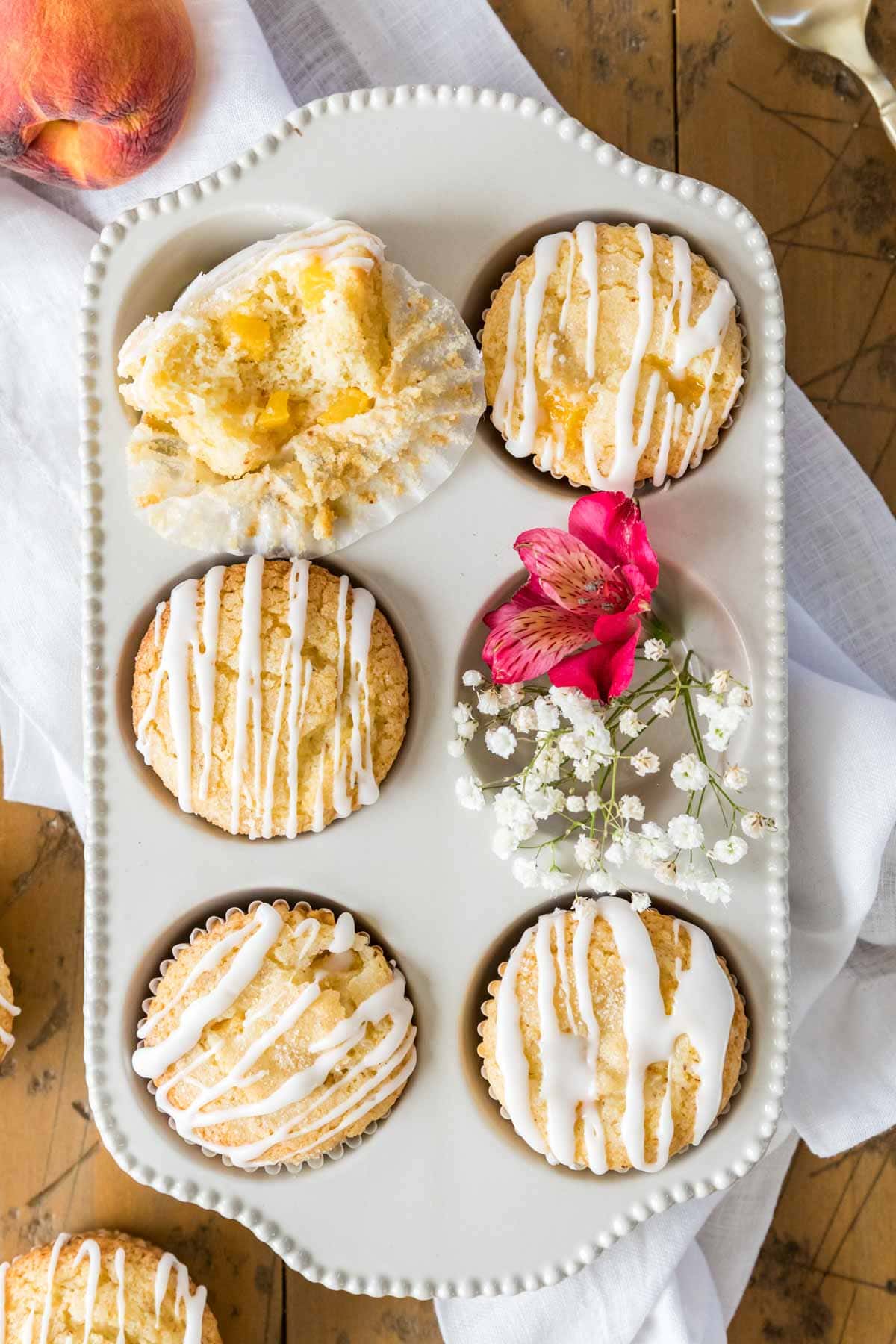Overhead view of a six count muffin tin filled with muffins, with the top left muffin missing a bite.