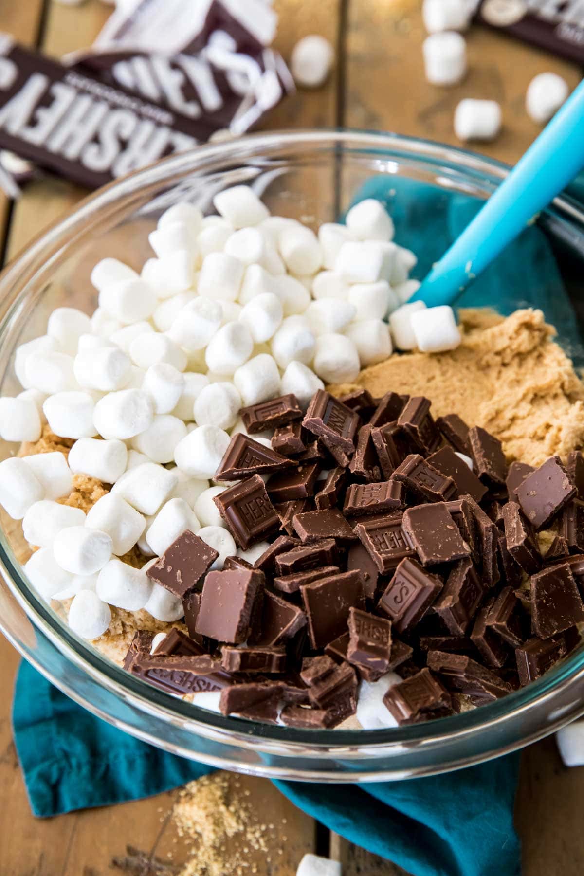 Bowl of cookie dough with mini marshmallows and broken up chocolate bars added on top before stirring.