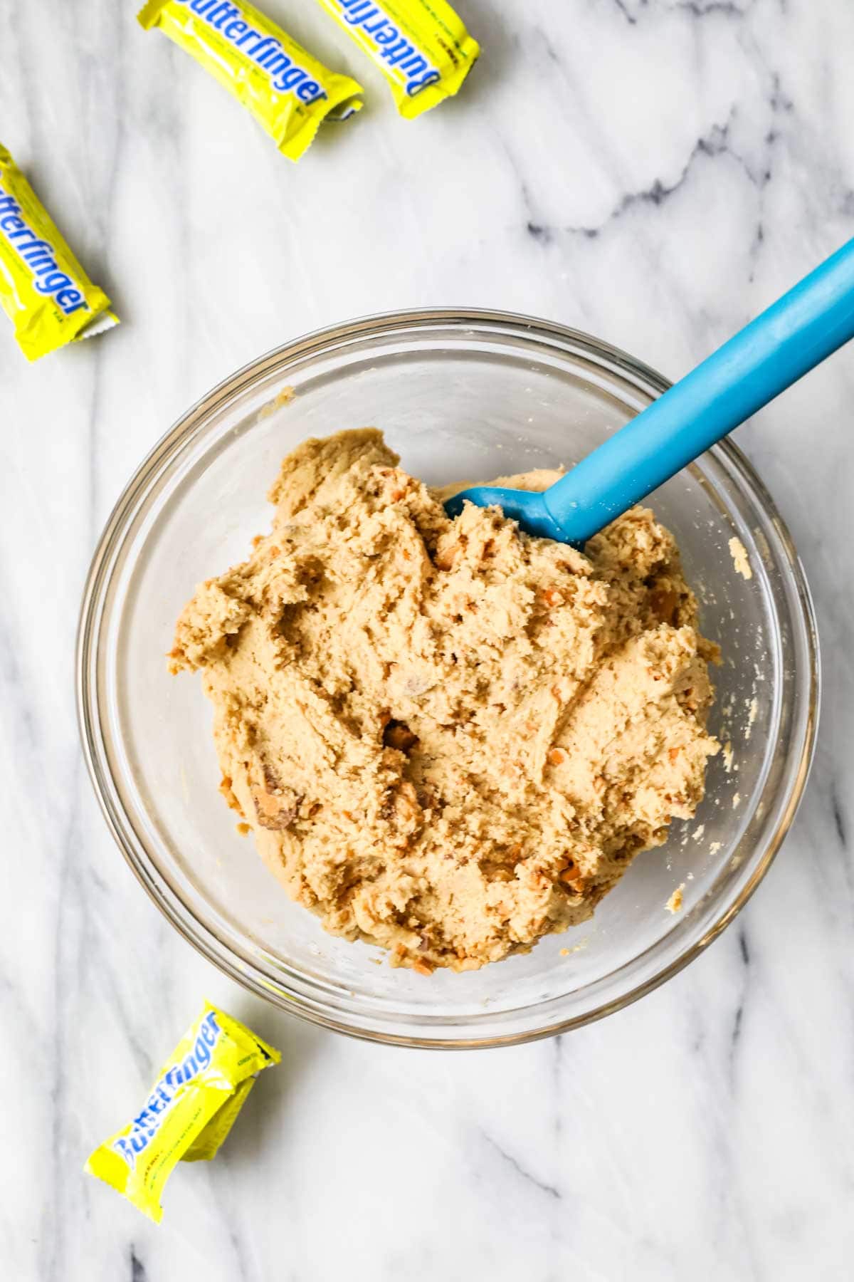 Overhead view of a bowl of cookie dough surrounded by fun size butterfinger candies.