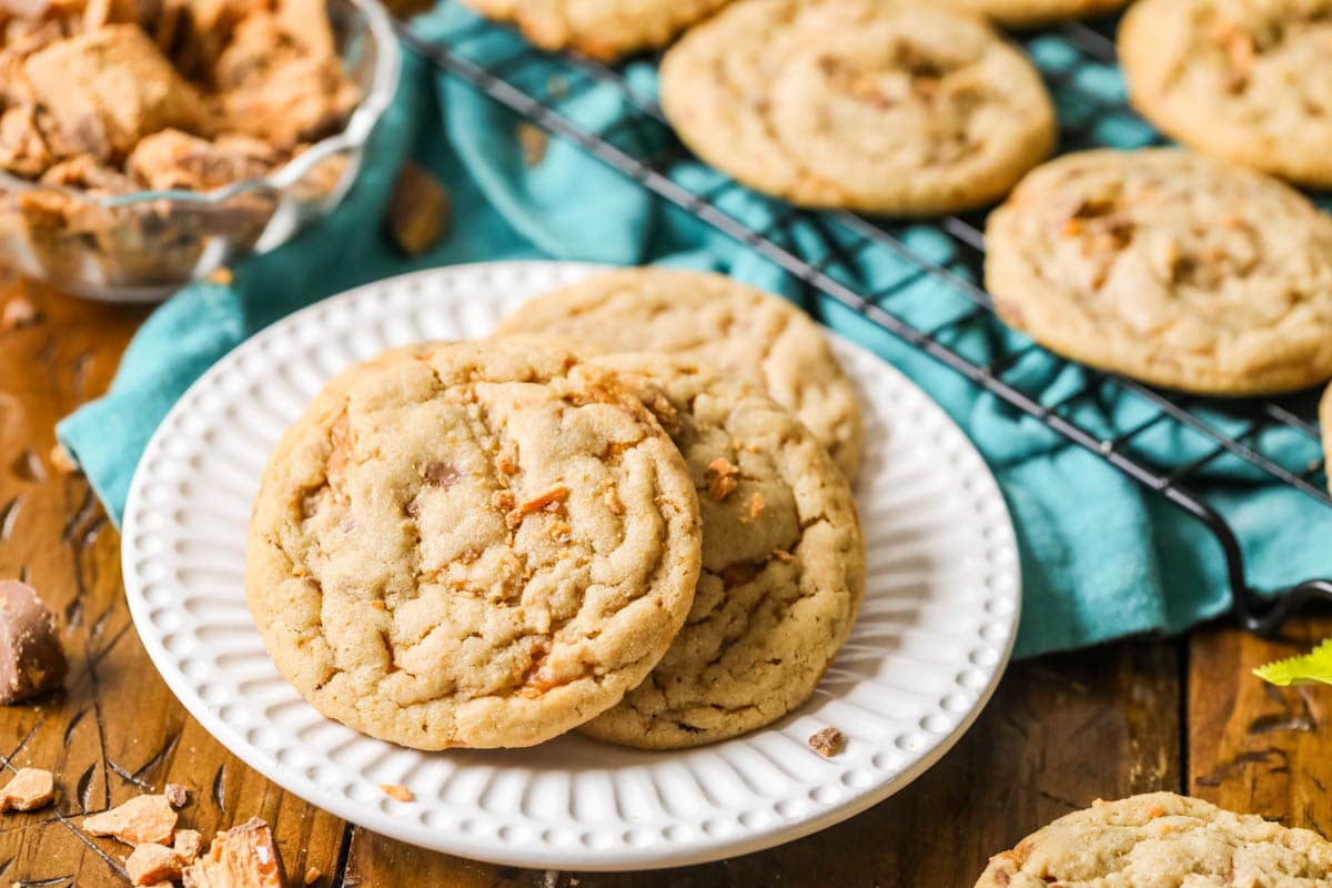 Several cookies studded with butterfinger pieces arranged on a white plate.
