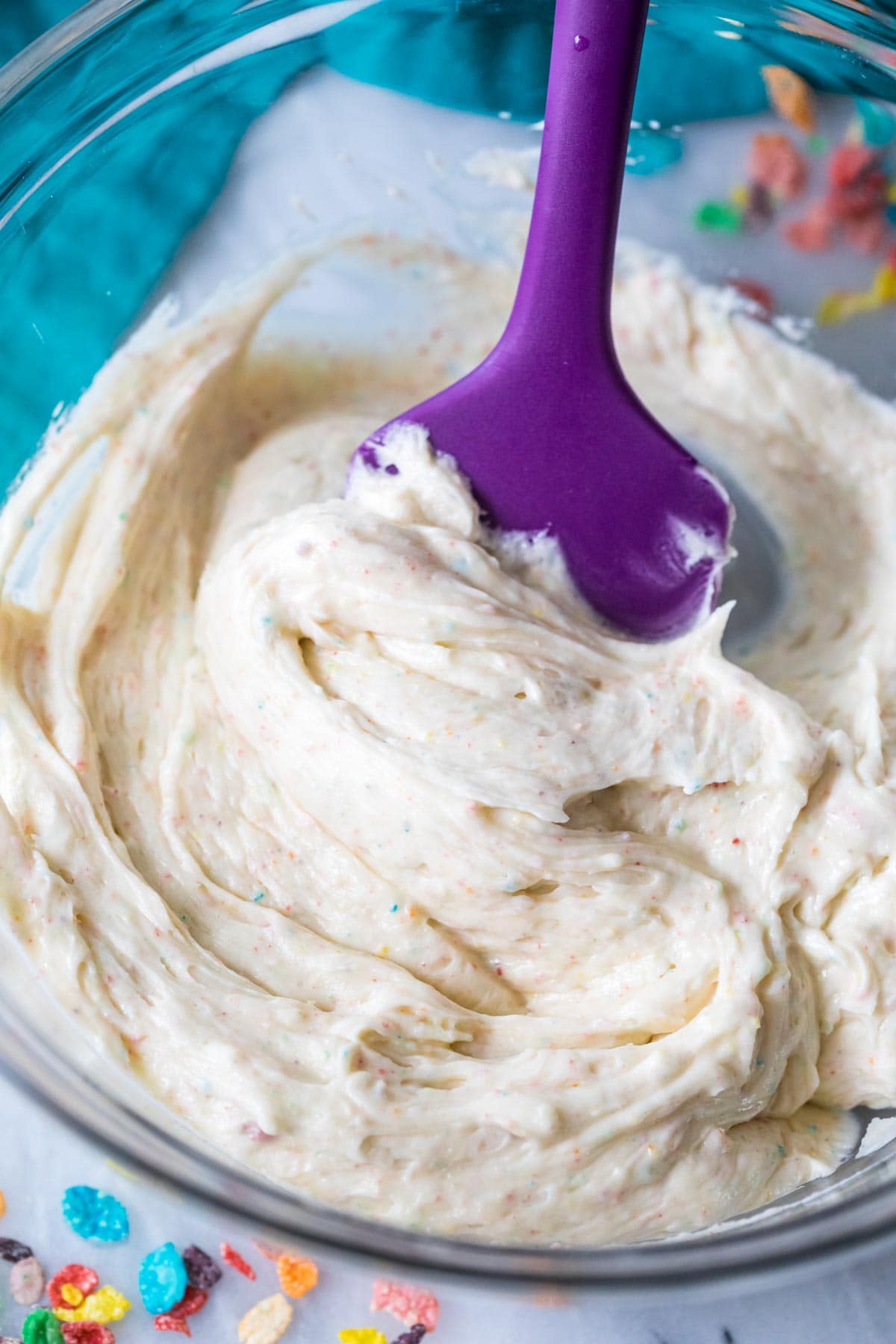 Spatula stirring a frosting made with fruity pebbles cereal.