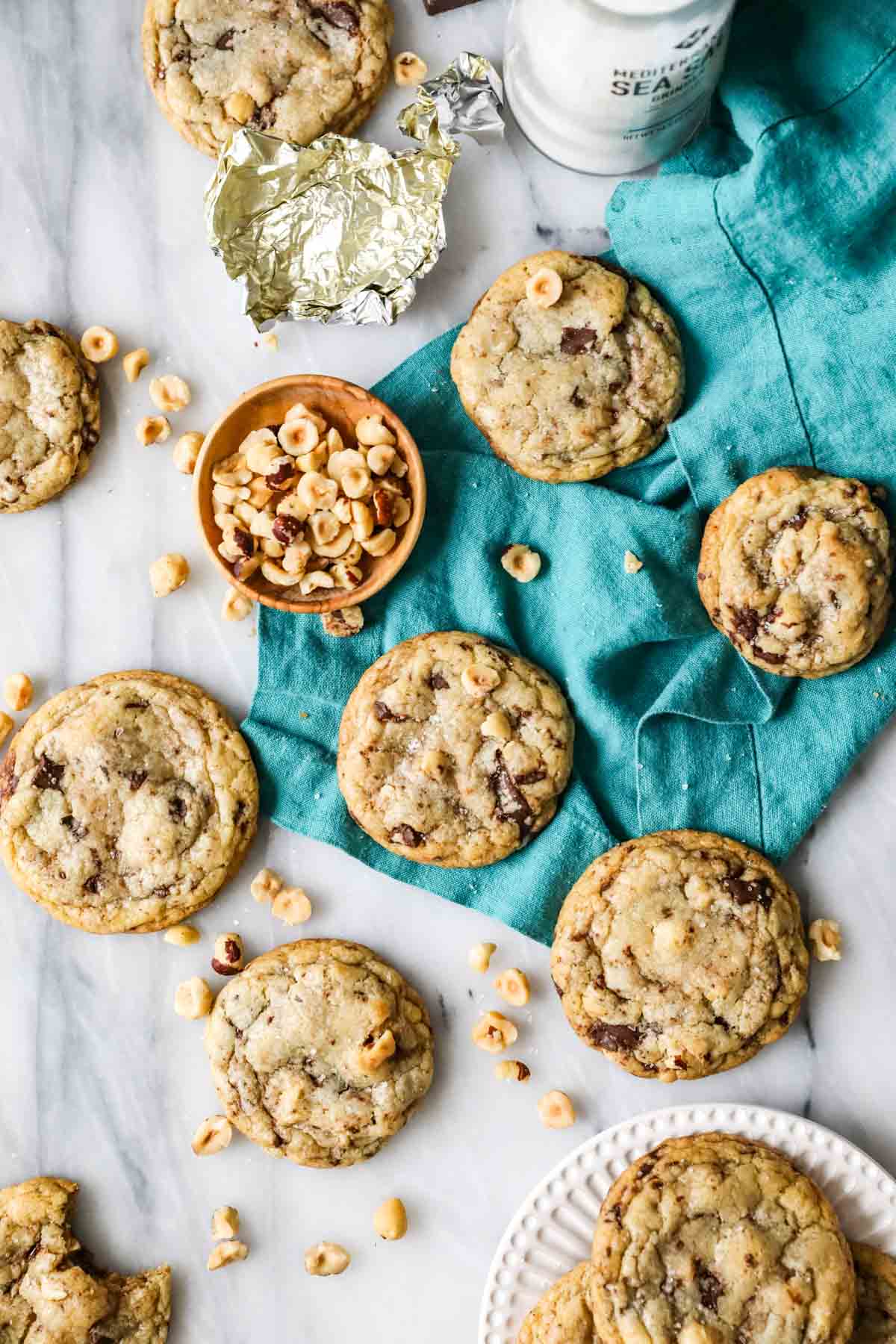 Overhead view of a teal tea towel with hazelnut chocolate chip cookies scattered across it.