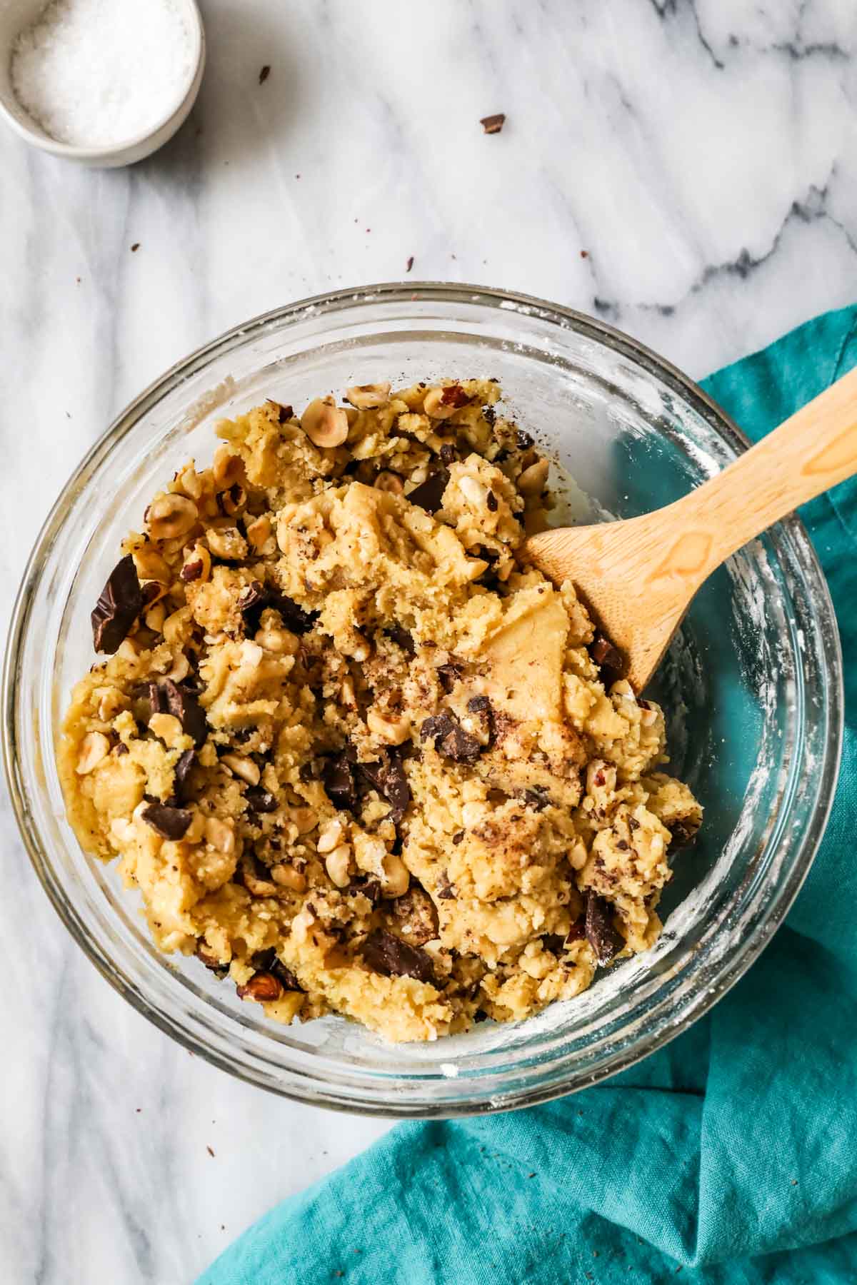 Overhead view of cookie dough studded with hazelnuts and chocolate chips in a bowl.