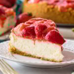 Slice of strawberry cheesecake on a plate with more cheesecake in the background.