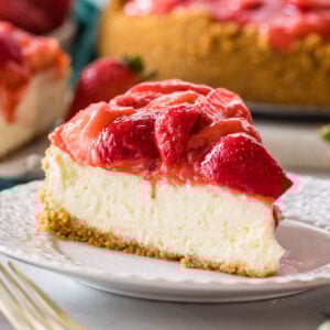 Slice of strawberry cheesecake on a plate with more cheesecake in the background.