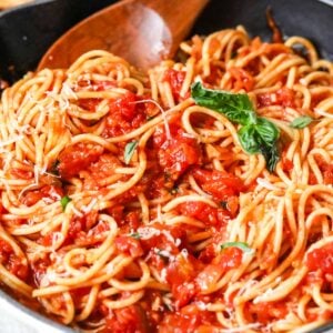 Pasta with arrabiata sauce being stirred by a wood spoon.