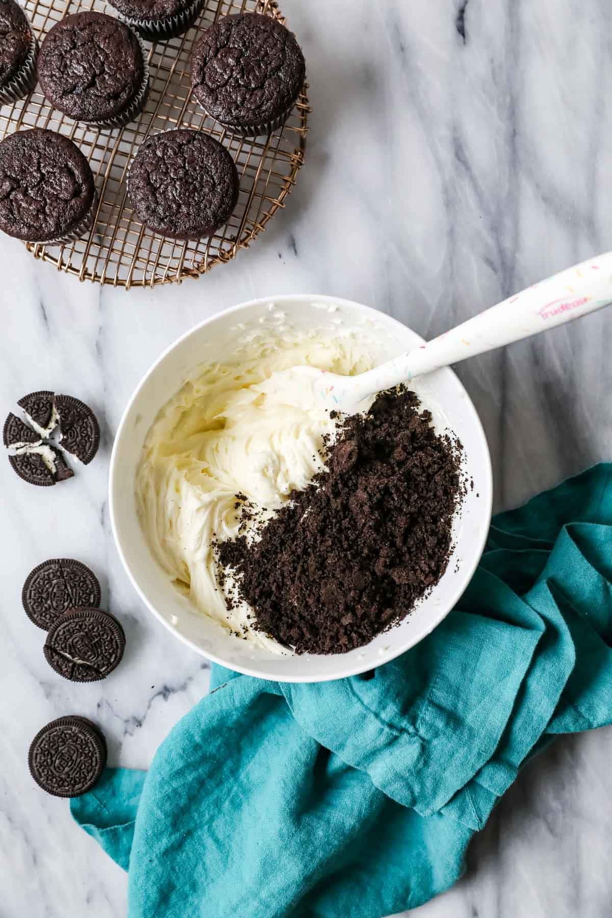 Overhead view of a bowl of frosting with Oreo cookie crumbs on top.