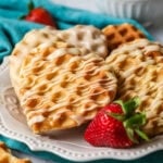 Heart shaped waffle cookies with a drizzled maple glaze on a white plate with a strawberry.
