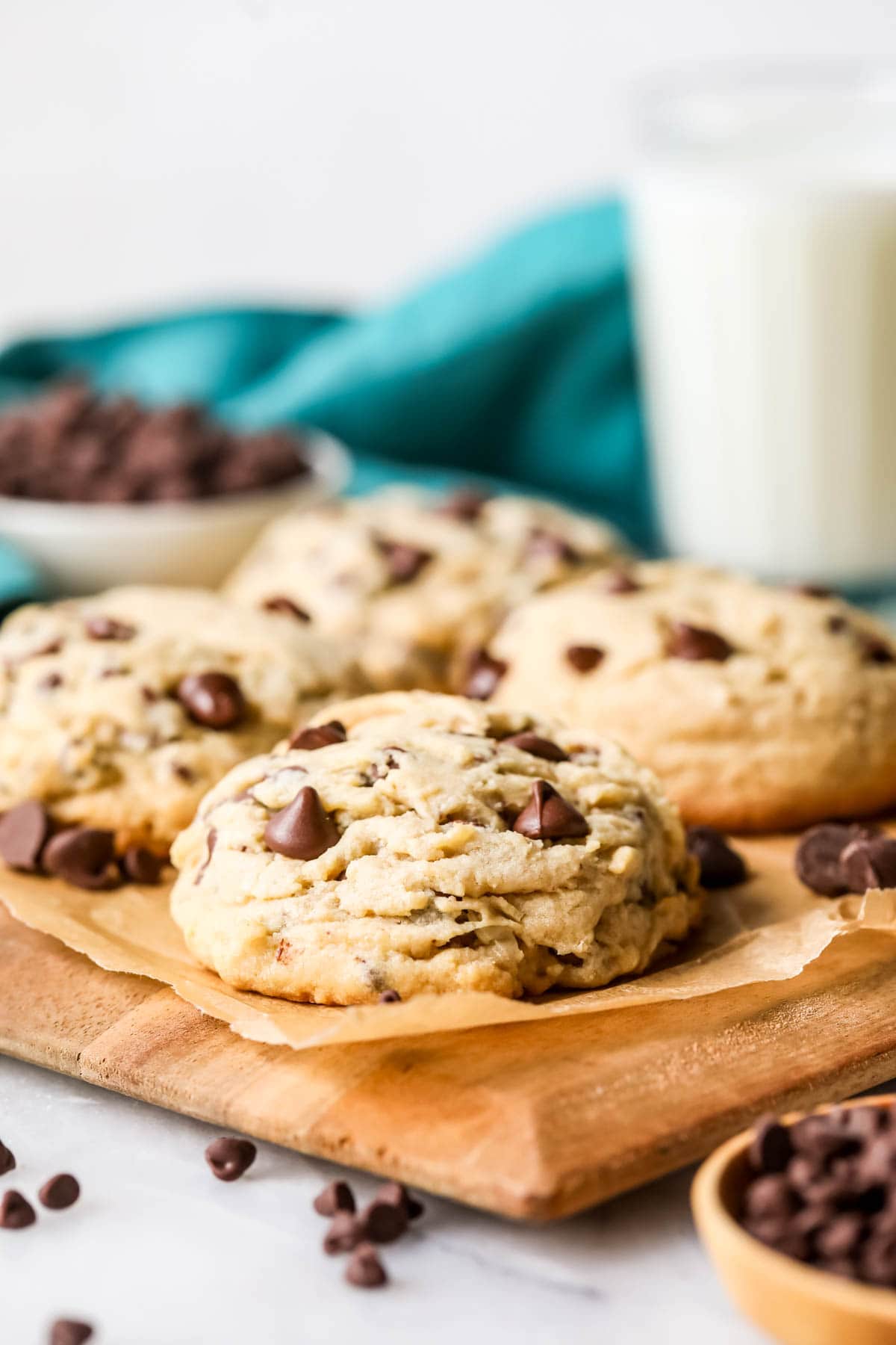 Thick, huge chocolate chip cookies on a wood cutting board.