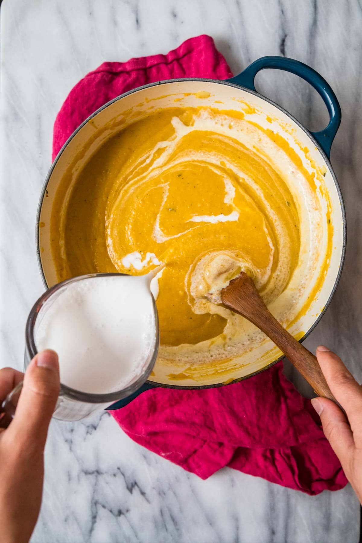 Overhead view of coconut milk being stirred into squash soup.